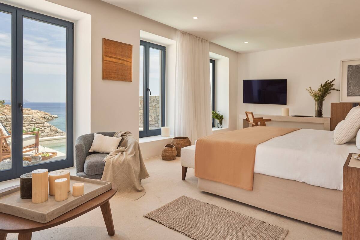 A modern hotel room with a large bed, a TV, and a view of the sea.
