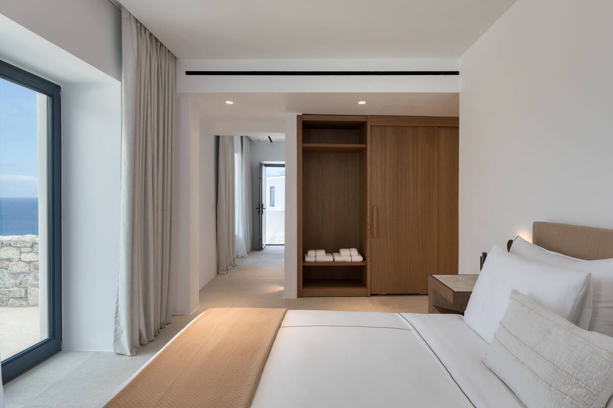 A modern hotel room with a large bed, a walk-in closet, and a view of the ocean.