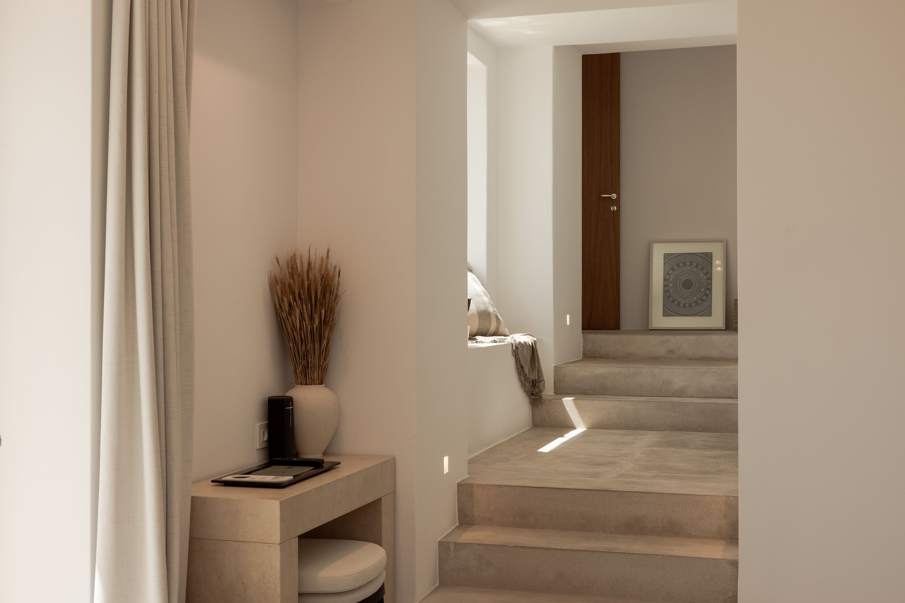 Un interior moderno con una escalera minimalista, una pequeña consola con un florero y una lámpara, y un cuadro en la pared.