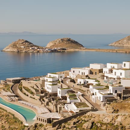 A coastal resort with white buildings, a swimming pool, and rocky terrain.