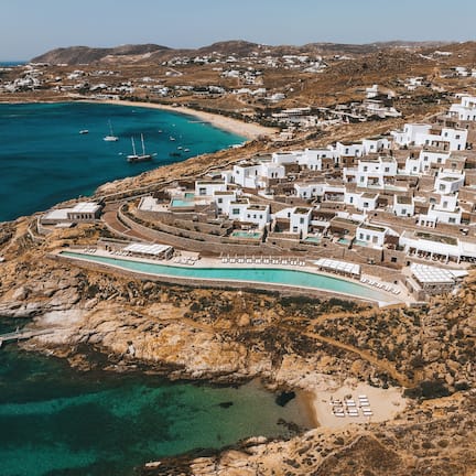 An aerial view of a coastal resort with a pool, boats, and white buildings.