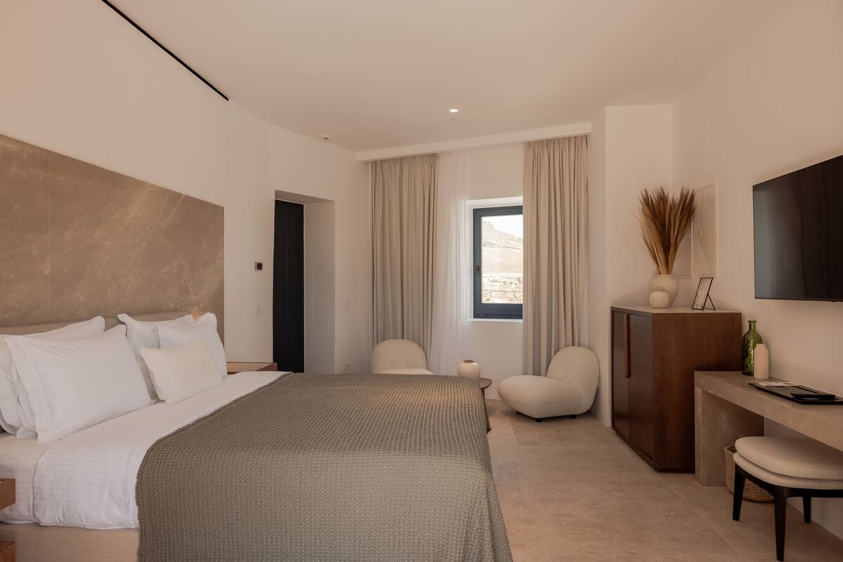 A modern bedroom with a large bed, a desk, a chair, and a TV.