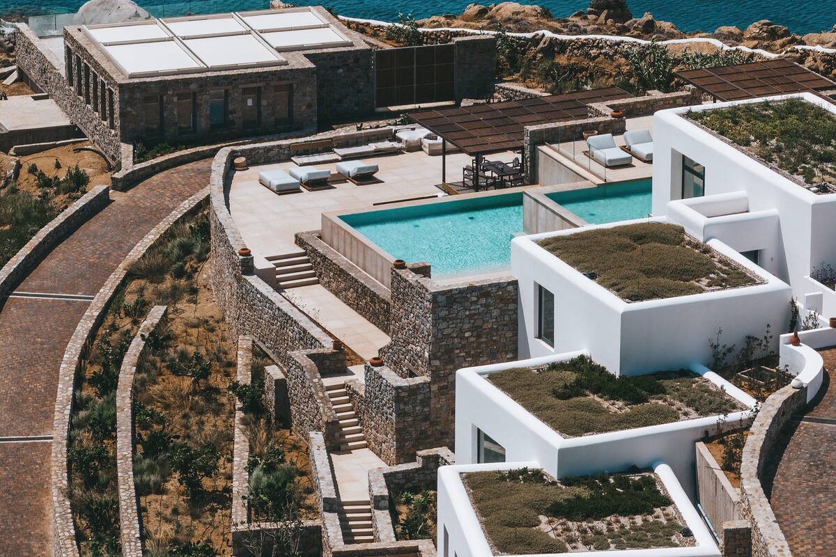 A modern villa with a rooftop pool, stone pathways, and a view of the sea.
