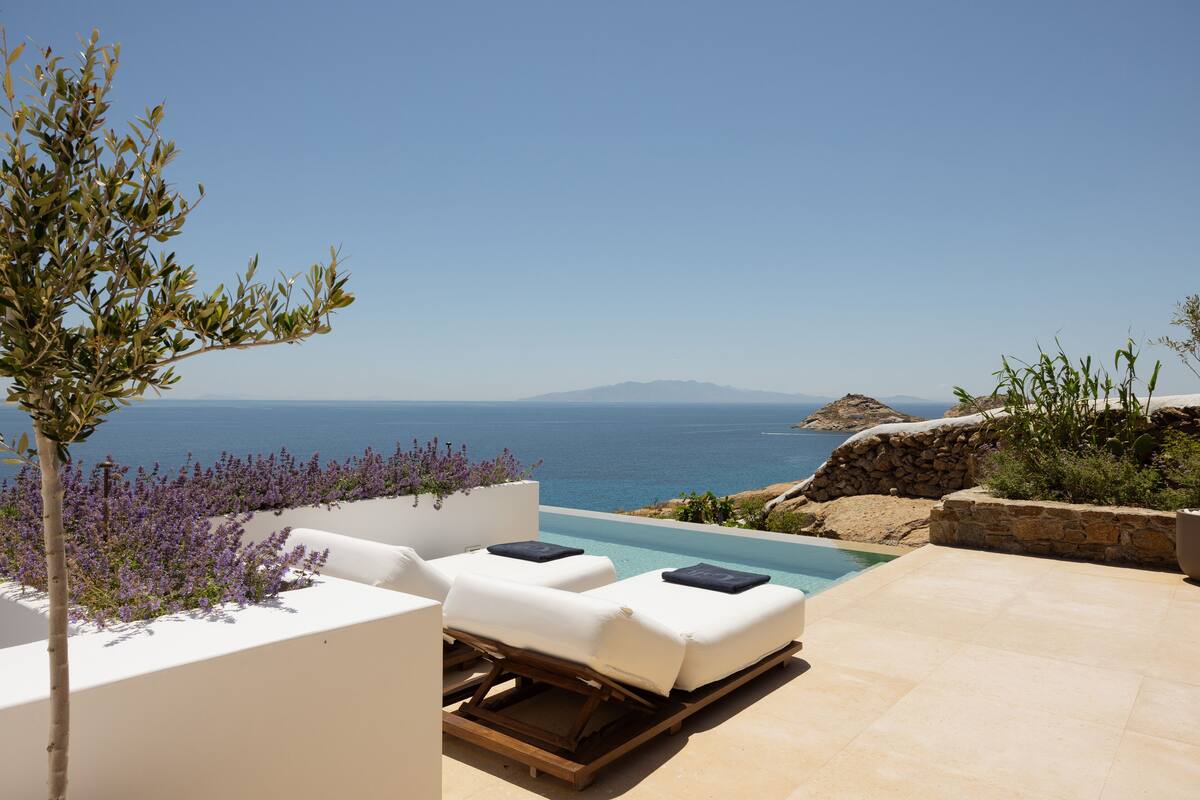 A poolside area with two sun loungers, a stone wall, and a view of the sea.