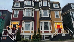 A row of Victorian-style townhouses with bay windows, a front porch, and a staircase leading to the entrance. - The Roses Heritage Inn (St. John's)