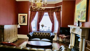 A traditional living room with a leather sofa, a fireplace, and a large window with curtains. - The Roses Heritage Inn (St. John's)