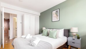 A modern bedroom with a bed, nightstand, and a door leading to another room.