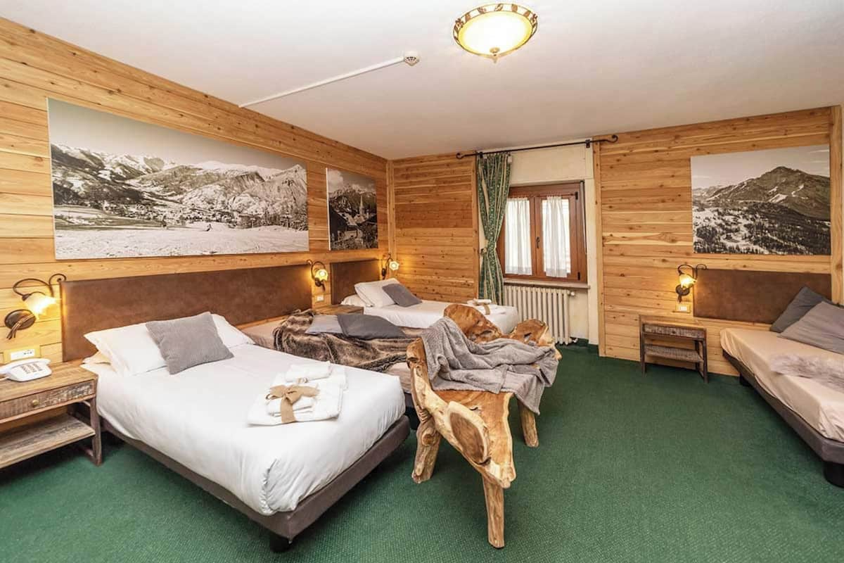 Quarto de hotel com duas camas, paredes de madeira e quadros com paisagens de montanha.