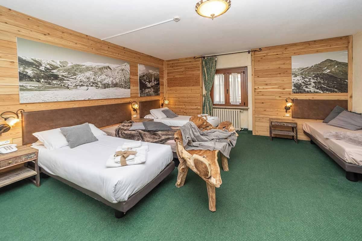 Quarto de hotel com decoração em madeira, uma cama grande, uma cama menor, uma cadeira de madeira e uma mesinha de cabeceira com abajur.