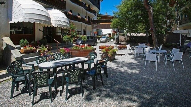 An outdoor patio with tables and chairs, surrounded by buildings and trees. - Hotel Gran Baita (Sauze d'Oulx)