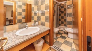 Un baño con piso a cuadros, lavamanos con espejo y zona de ducha.