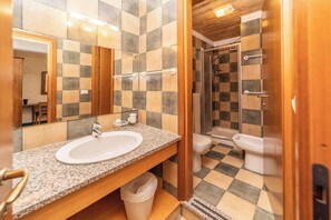 Un baño con piso a cuadros, lavamanos con espejo y zona de ducha.