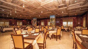 A large banquet hall with multiple round tables set for dining, wooden paneling on the ceiling, and large windows with curtains. - Hotel Gran Baita (Sauze d'Oulx)