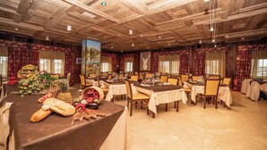 Un amplio salón de banquetes con múltiples mesas dispuestas para comer, con un techo rústico de madera y un cuadro grande en la pared.
