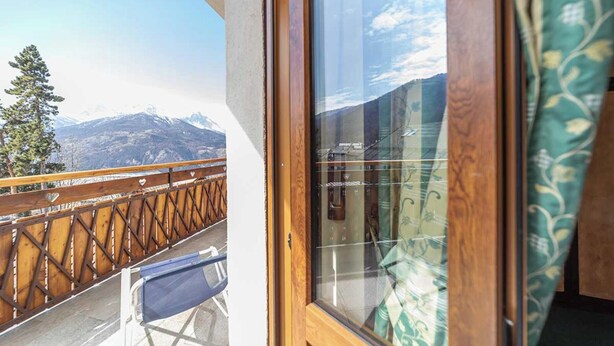 Un balcón con barandilla de madera y vista a las montañas.