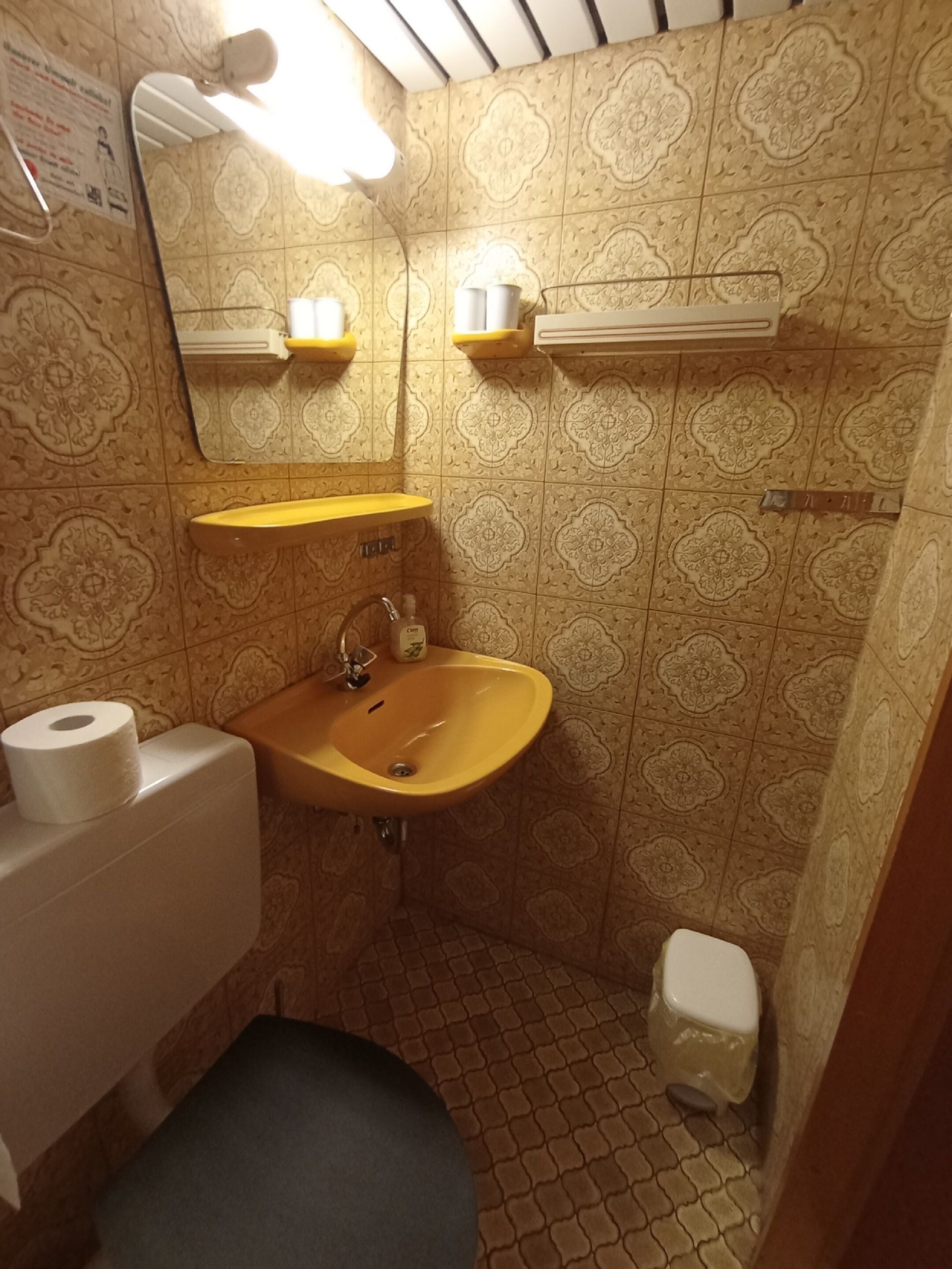 Un baño con azulejos estampados, un lavabo amarillo, un inodoro y un espejo.