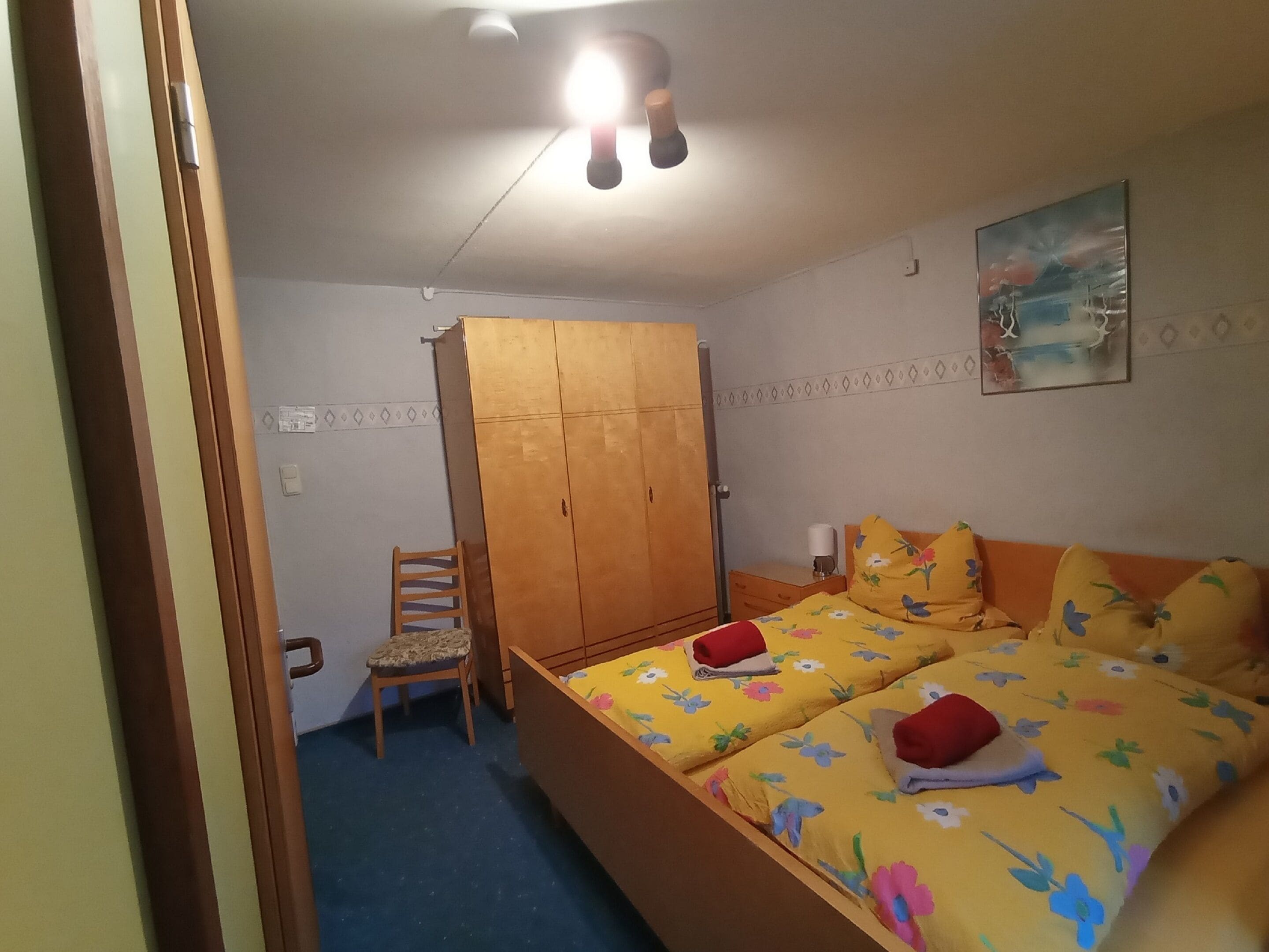 Quarto com cama, uma cadeira, guarda-roupa e um quadro na parede.