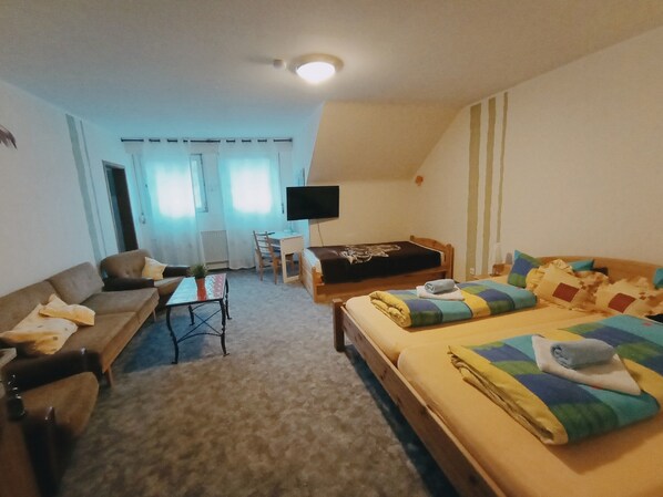 A room with a bed, a sofa, a small table with a plant, a TV, and a window with curtains. - Hotel Gasthof Müller (Winterberg)