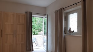 A bedroom with a large wooden wardrobe, a sliding glass door leading to an outdoor area, and a window with a decorative item.
