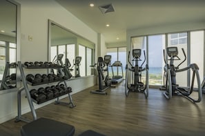 Une salle de sport équipée de matériel d’exercice, avec un porte-haltères et de grandes fenêtres donnant sur un paysage agréable.
