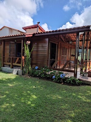 Ein Holzhaus mit überdachter Veranda, ein kleiner Garten mit blauen Blumen und einem klaren Himmel.