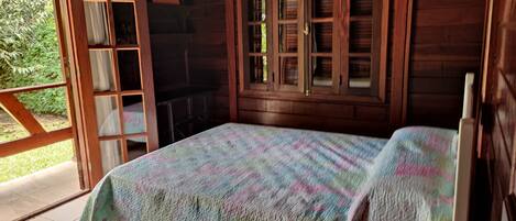 Una habitación de cabaña de madera con una cama, una ventana con contraventanas y una puerta que da al exterior.