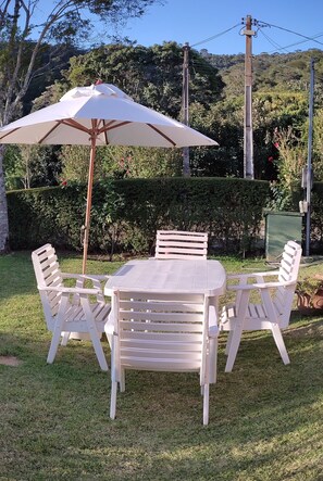Eine Terrasse mit Tisch und Stühlen, umgeben von einem gepflegten Garten und einem Hecken.