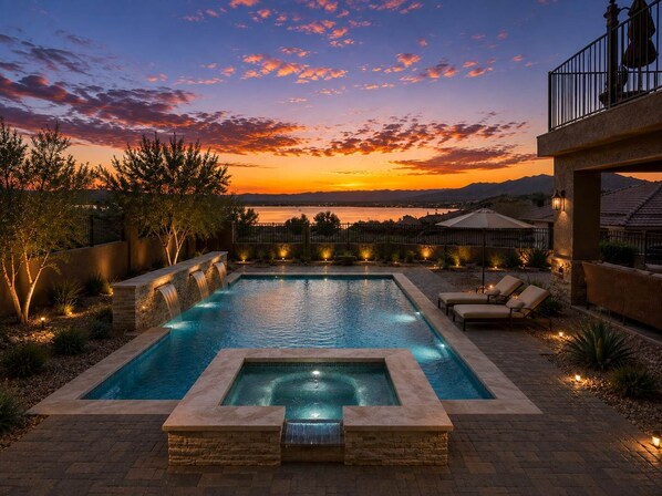 A rectangular swimming pool with a waterfall feature, surrounded by stone walls and outdoor lighting.