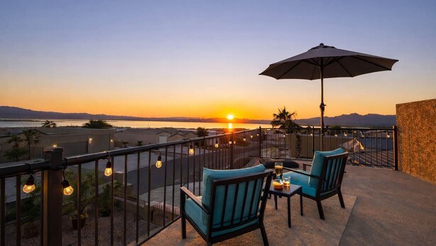 Ein Balkon mit zwei Stühlen und einem Tisch, der Blick auf einen Sonnenuntergang über Wasser und Berge bietet.