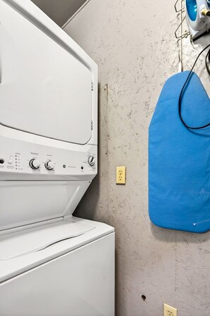 Lavadora y secadora blancas en un lavadero con pared texturizada y una bolsa de ropa azul colgada en un tendedero.