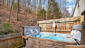 A hot tub in a backyard with a wooden fence, stone wall, and a sign indicating hot tub rental. - Lazy Lane Cabins - Brookside Cabin (South Bloomingville)