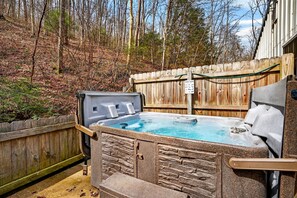 A hot tub in a backyard with a wooden fence, stone wall, and a sign indicating hot tub rental.
