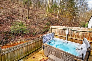 Un jacuzzi en un patio trasero con valla de madera y árboles al fondo.