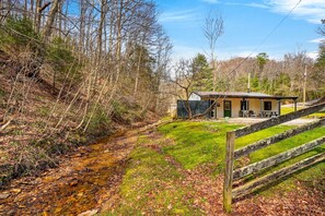 A rustic cabin with a porch, a small shed, and a stream.