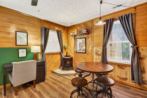 A cozy room with a wooden interior, a round table with stools, a small stove, and a desk with a chair.