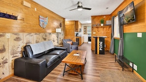 A cozy room with a leather sofa, wooden coffee table, and a kitchen area in the background. - Lazy Lane Cabins - Brookside Cabin (South Bloomingville)