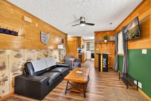 Una habitación acogedora con un sofá de cuero, una mesa de centro de madera y una zona de cocina al fondo.