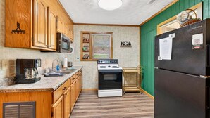 A kitchen with wooden cabinets, a stove, a refrigerator, and a microwave. - Lazy Lane Cabins - Brookside Cabin (South Bloomingville)
