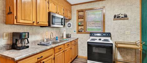 A kitchen with wooden cabinets, a microwave, a stove, a coffee maker, and a window with blinds.