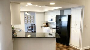 Une cuisine moderne avec des meubles blancs, un réfrigérateur noir et un plan de travail en granit.