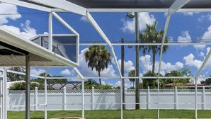 Un espace extérieur abrité, avec une clôture blanche, des palmiers et un ciel d’un bleu limpide.
