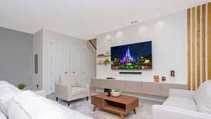 Een moderne woonkamer met een flatscreen tv aan de muur, een bank, een salontafel en een trap die naar een ander niveau leidt.