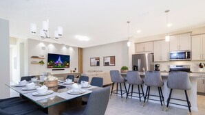 Een moderne keuken met een magnetron, koelkast en een eetgedeelte met een glazen tafel en barkrukken.