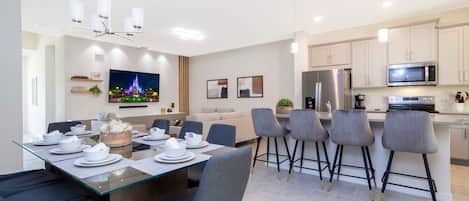 Una cocina moderna con microondas, refrigerador y comedor con mesa de vidrio y taburetes de bar.