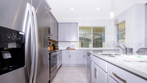 Een moderne keuken met witte kastjes, roestvrijstalen apparatuur en een groot raam met zonwering.