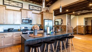 A modern kitchen with wooden cabinets, a central island with bar stools, stainless steel appliances, and a rustic ceiling. - Luxury Smoky Chalet, Indoor Pool, Hot Tub, Theater,  Sleep 12 in 4 King Suites, Indoor Fireplace, Outdoor Fire Pit, Game Loft & Scenic Views, 20 Min to Dollywood, The Island & Parkway, Dog-Friendly, 24 Hr Hospitality (Sevierville)