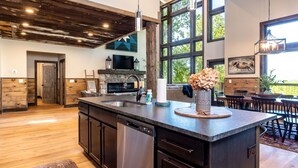 A modern kitchen with a large island, built-in dishwasher, and a stone fireplace. - Luxury Smoky Chalet, Indoor Pool, Hot Tub, Theater,  Sleep 12 in 4 King Suites, Indoor Fireplace, Outdoor Fire Pit, Game Loft & Scenic Views, 20 Min to Dollywood, The Island & Parkway, Dog-Friendly, 24 Hr Hospitality (Sevierville)