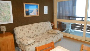 Ein gemütliches Wohnzimmer mit einem gemusterten Sofa, einem Holzkabinett und einem Esstisch.