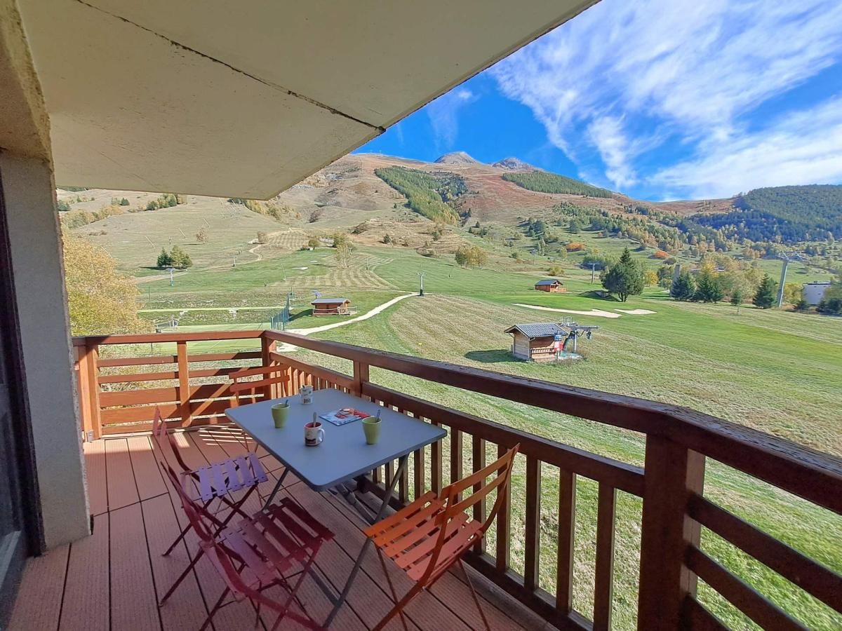 A balcony with a table and chairs, overlooking a rural landscape with fields and hills.