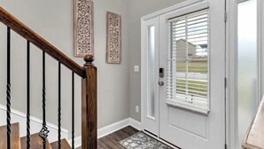 Una escalera con barandilla de madera y balaustradas negras, una puerta blanca con un ventanal y dos paneles decorativos en la pared.